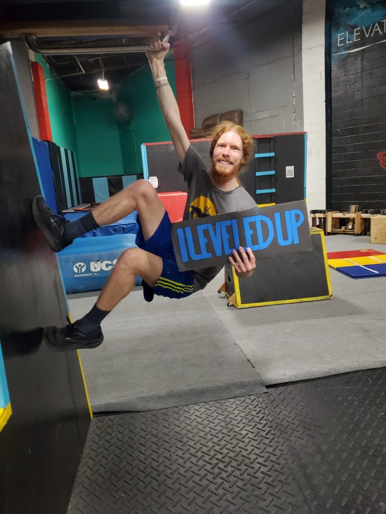 A student holding a Level Up sign while hanging from an overhead bar