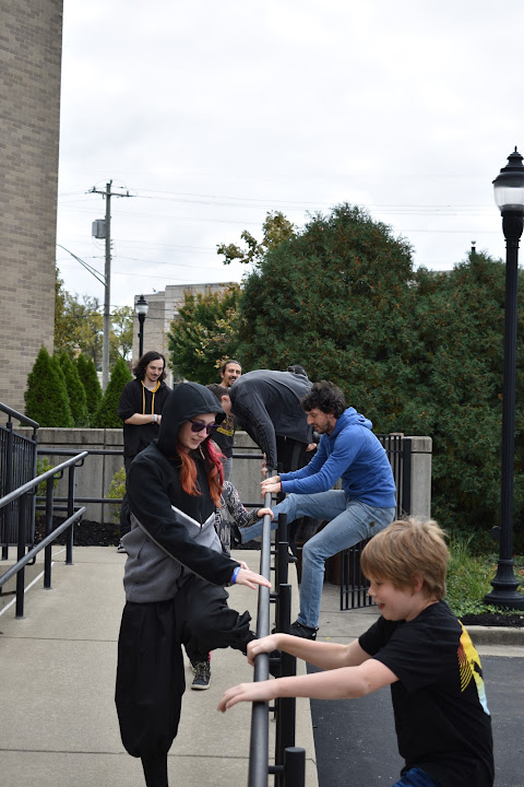 Adults and a child practicing movement around an outdoor handrail.