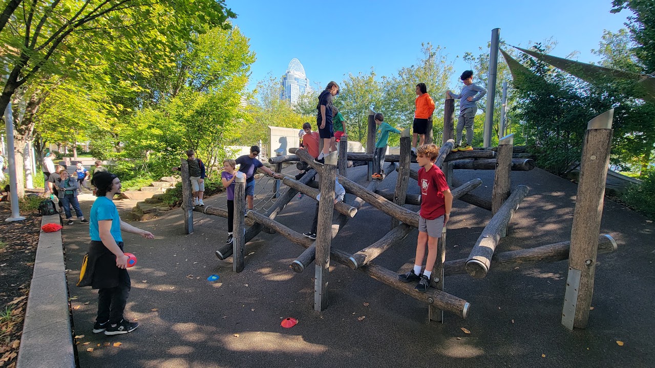 Children practicing balance on wooden beams at an outdoor CincyJam gathering.