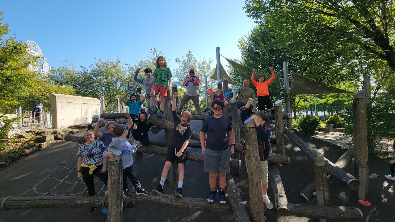 Children and adults smiling together on a wooden climbing structure at CincyJam 2025.